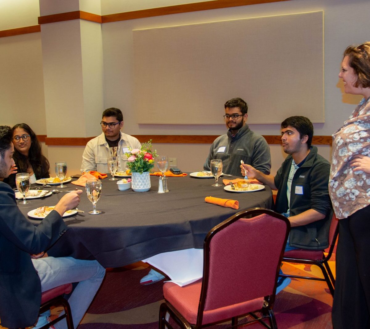 Michelle Seref (standing at right), Pamplin's interim assistant dean of outreach and student engagement, talks with students at the luncheon. The students include (clockwise from left) Anay Maheshwari, Sanjana Mehta, Isha Ghatule, Shubh Patel, Abhay Pai, and Sharmad Samant. Photo by Amanda Broome for Virginia Tech.