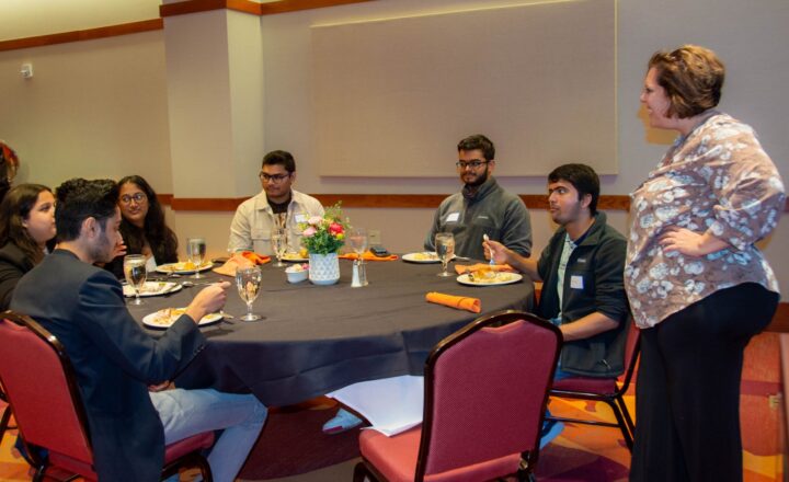Michelle Seref (standing at right), Pamplin's interim assistant dean of outreach and student engagement, talks with students at the luncheon. The students include (clockwise from left) Anay Maheshwari, Sanjana Mehta, Isha Ghatule, Shubh Patel, Abhay Pai, and Sharmad Samant. Photo by Amanda Broome for Virginia Tech.